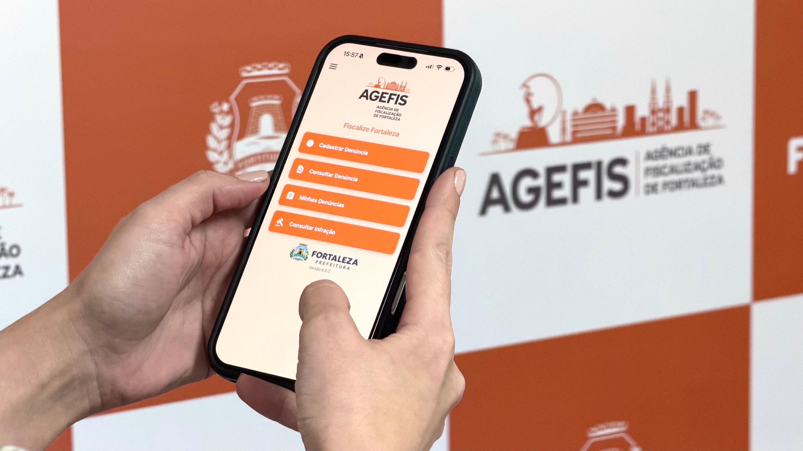 A foto mostra um celular nas mãos de uma pessoa. Na tela aparece o canal de denúncia da Agefis